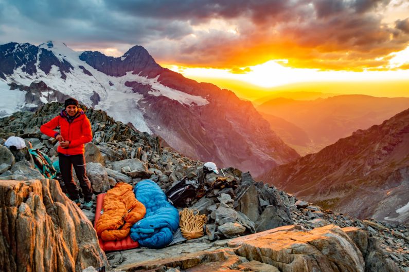 Bivy - person in red jacket and blue denim jeans sitting on rock near snow covered mountain during