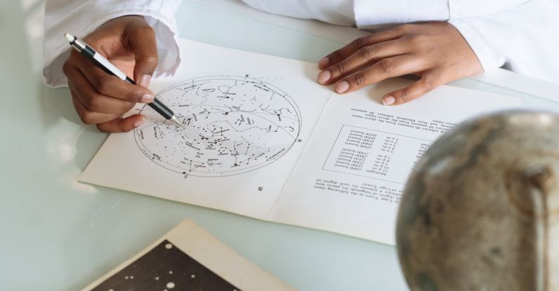 Modify - Crop of focused scientist wearing white uniform and modifying constellation map while sitting at table with globe and educational materials in university